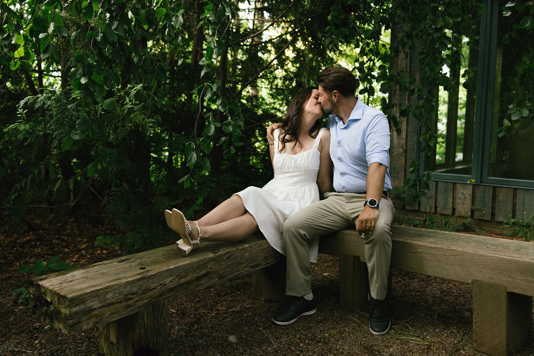 Danielle and Brenden kissing while seated on a garden bench